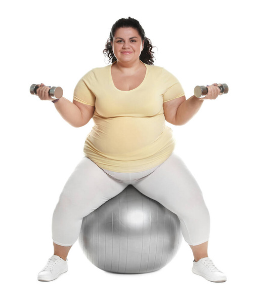 Overgewicht vrouw doet oefening op fit bal met halters tegen witte achtergrond - Foto, afbeelding