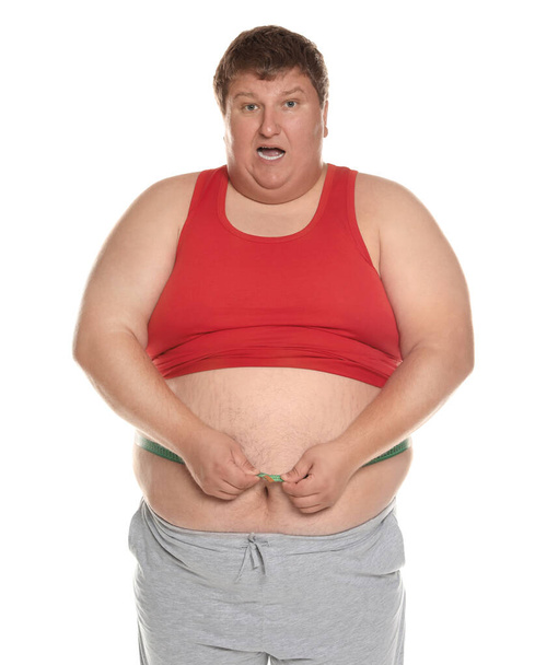 Emotional overweight man measuring waist with tape on white background - Zdjęcie, obraz