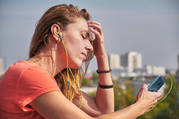 Woman with headphones on, listening to a song on her phone and looking sad with her eyes closed. - Φωτογραφία, εικόνα