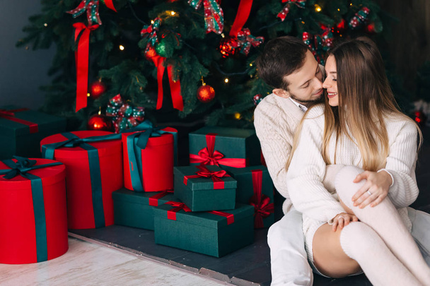 coppia seduta vicino all'albero di Natale e regali in maglia bianca - Foto, immagini
