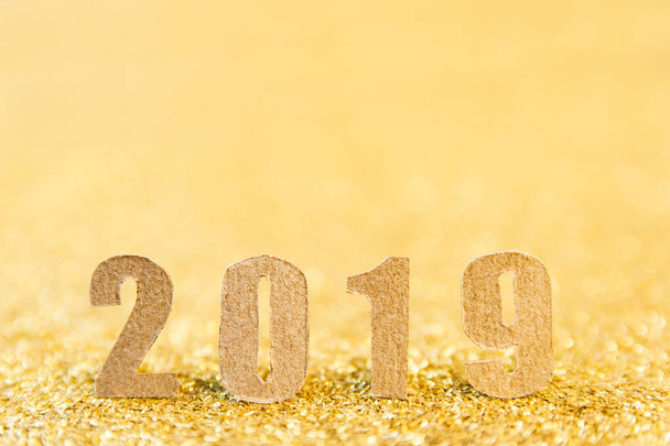 2019 Neujahrstext mit braunem Papier auf goldenem Glitzerhintergrund.  - Foto, Bild