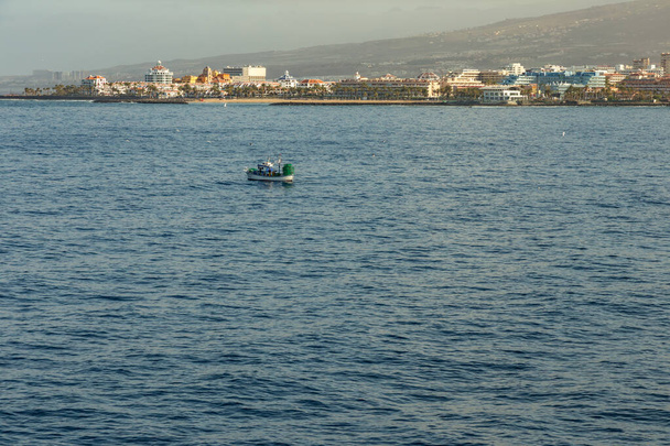 Las Americas, Tenerife, Spain - May 25, 2019: Θέα στην ακτογραμμή και ένα μικρό αλιευτικό πλοίο από το πλοίο που αναχωρεί για το νησί La Gomera νωρίς το πρωί από το λιμάνι του Los Cristianos - Φωτογραφία, εικόνα