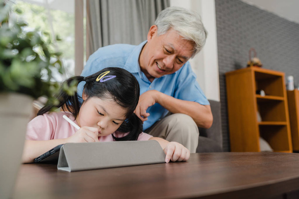 Aasialainen isoisä opettaa lapsenlapsi piirustus ja kotitehtäviä kotona. Vanhempi kiinalainen, isoisä onnellinen rentoutua nuori tyttö makaa sohvalla olohuoneessa kotona käsite. - Valokuva, kuva