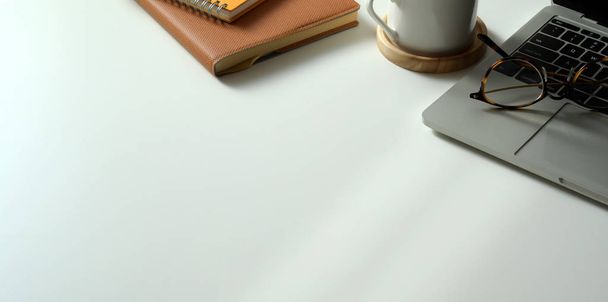 Обрізаний знімок сучасного робочого місця з портативного комп'ютера, книг та офісних приладдя з копіювальним простором на білому столі фоні
 - Фото, зображення