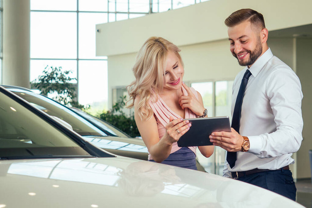 salesman in suit showing catalog to female blonde customer in dealership salon - Photo, Image