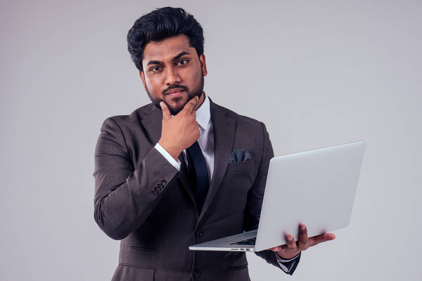 Portrait of bearded Indian male holds a laptop at studio on white background - Фото, изображение