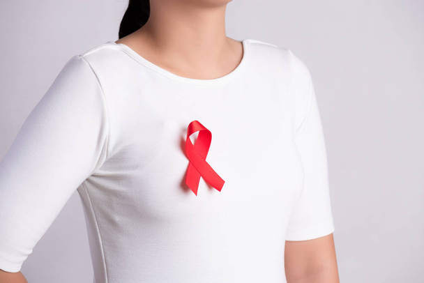 Detailní záběr na červenou stuhu s odznakem na ženské hrudi na podporu dne AIDS. Zdravotní péče, medicína a koncepce povědomí o AIDS. - Fotografie, Obrázek