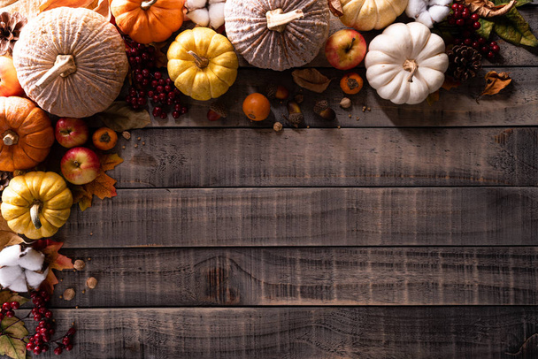 Vista superior de las hojas de arce de otoño con calabaza y bayas rojas sobre fondo de madera oscura. Concepto del día de Acción de Gracias
. - Foto, imagen