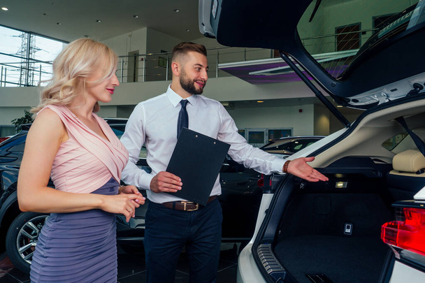 caucasian salesman in suit showing catalog to beautiful female blonde well-dressed customer in dealership salon - Photo, Image
