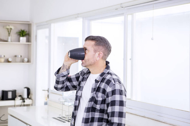 Молодой человек пьет чашку кофе на кухне
 - Фото, изображение