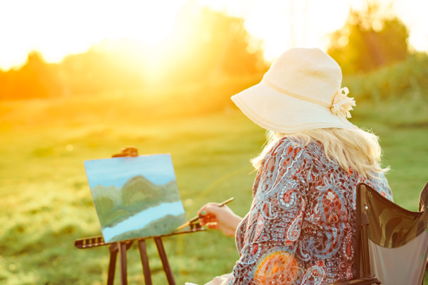 μια ηλικιωμένη γυναίκα ζωγραφίζει μια εικόνα στη φύση - Φωτογραφία, εικόνα