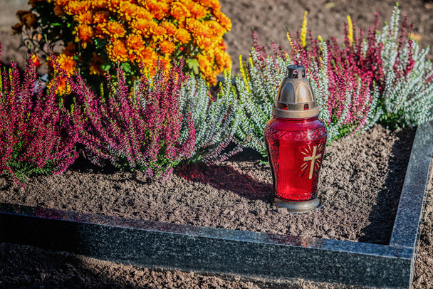 Κόκκινο φανάρι με κερί και λουλούδια στον τάφο στο νεκροταφείο - Φωτογραφία, εικόνα