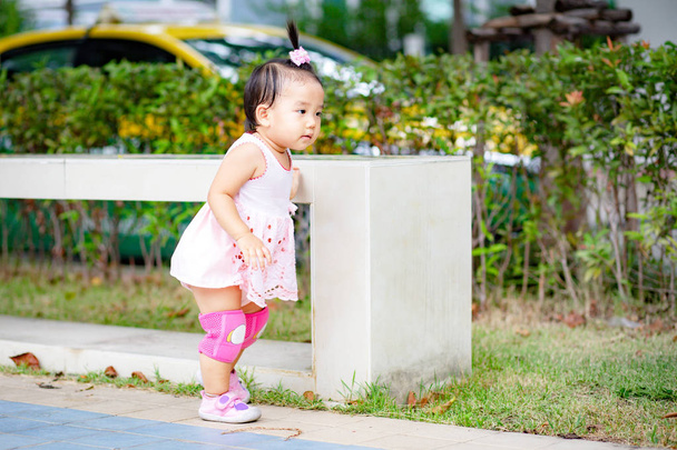 Kleines Mädchen in rosa Kleid und Knieschoner läuft auf Fußweg im Park - Foto, Bild