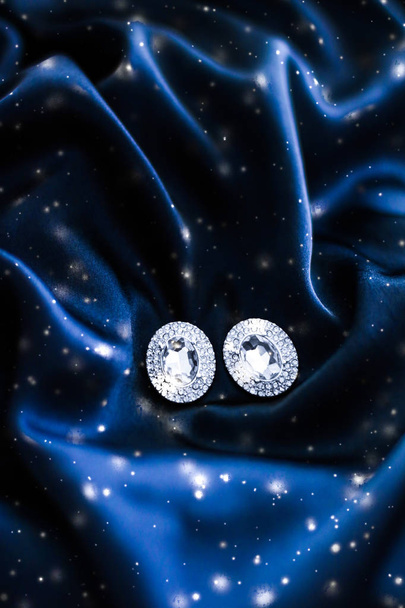 Πολυτελή διαμαντένια σκουλαρίκια σε σκούρο μπλε μετάξι με γκλίτερ χιονιού, - Φωτογραφία, εικόνα