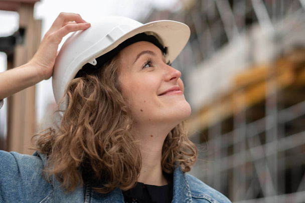 Nahaufnahme Porträt einer netten und jungen Ingenieurin mit weißem Schutzhelm, die auf etwas über ihr blickt. Selektiver Fokus - Foto, Bild
