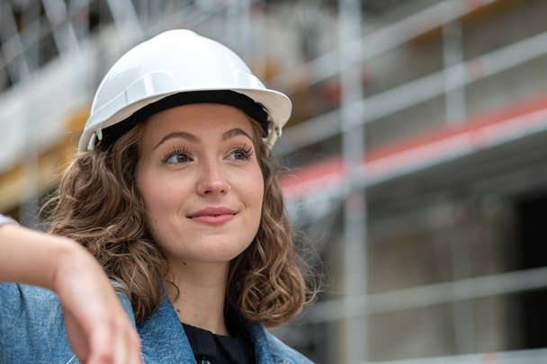 Close up portrait of a pretty and young female engineer wearing a white protective helmet - Photo, Image