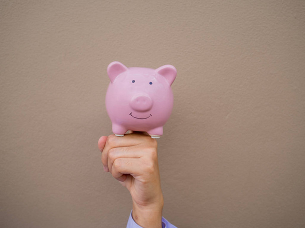 Empresários mão segurando rosa porquinho banco no fundo parede de cimento marrom, Economizando dinheiro para o futuro plano e conceito de fundo de aposentadoria
 - Foto, Imagem