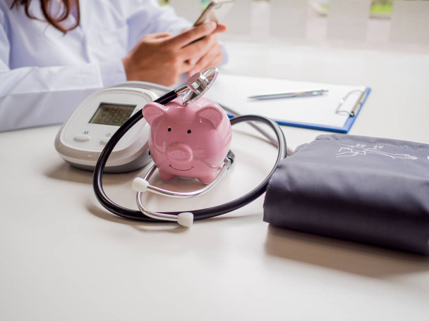 rosafarbenes Sparschwein mit Doktor-Stethoskop und Manometer, das Geld für Zukunftskonzept und Krankenkassenkonzept spart - Foto, Bild