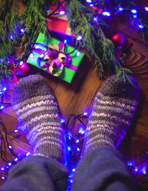 Στέκομαι σε πλεκτές κάλτσες κοντά στο χριστουγεννιάτικο δέντρο με δώρα. - Φωτογραφία, εικόνα