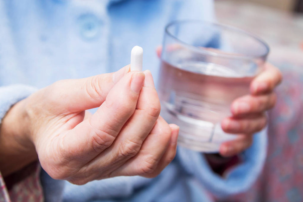 woman with pills or capsules on hand and a glass of water - Photo, image