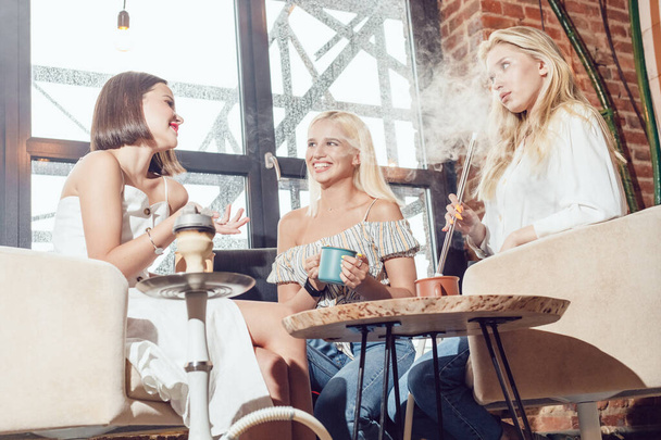 Три дівчини-подружки сидять в кафе, спілкуються і курять кальян
. - Фото, зображення