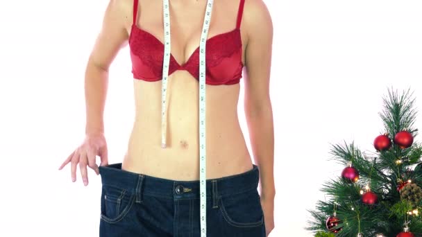 Magere vrouw in rode beha met meetlint met grote broek en appel. Concept van dieet, gewichtsverlies en lichaamscontrole, vet en slank worden tijdens kerstvakantie, goede bedoelingen - Video