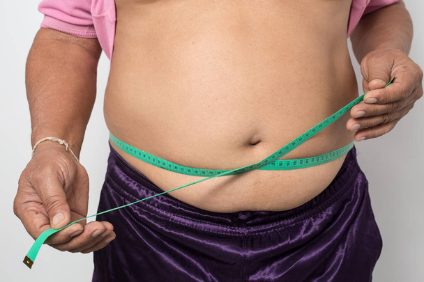 Υπερβαρών άνθρωπος ελέγξτε το σωματικό λίπος του με πράσινη ταινία μέτρησης για την παχυσαρκία σε γκρι φόντο, Υγιής έννοια  - Φωτογραφία, εικόνα