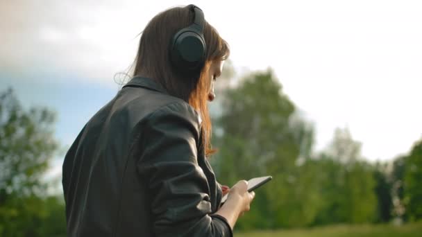Lány, zenét hallgat wi-fi fejhallgató okostelefonnal, sétál a parkban a kutyájával. - Felvétel, videó