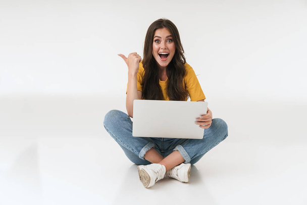 Emotional surprised cheery young woman isolated over white wall background using laptop computer pointing. - Foto, Imagem