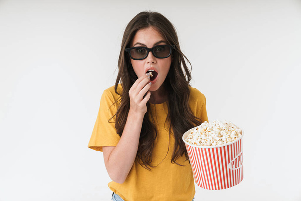 Concentrated young woman isolated over white wall background in 3d glasses eat popcorn watch film. - Foto, Imagem