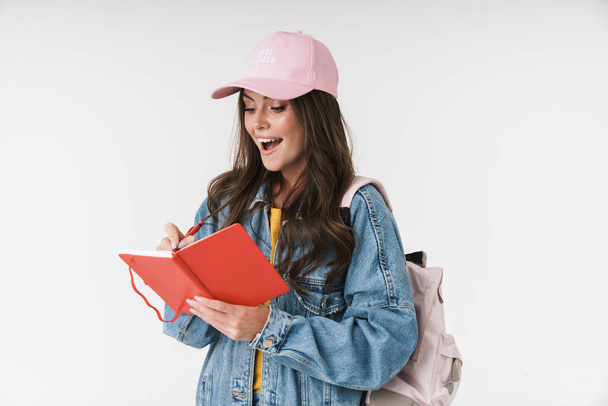 Photo of pretty student girl wearing cap smiling while writing d - Foto, Imagem