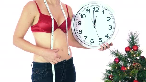 Nainen punaisissa rintaliiveissä lihoo joululomien aikana, näyttää kelloa ja peukaloa alaspäin. Käsitys laihduttaa ja aikaa, ei lykätä tai lykätä ruokavaliota, laskea alas ja hyviä aikomuksia uudelle vuodelle
 - Materiaali, video