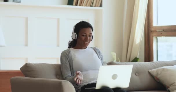 Happy african woman wear headphones making video call on laptop - Materiaali, video