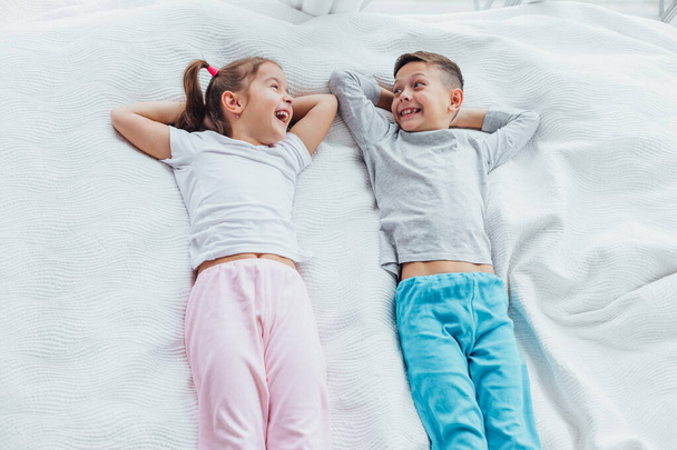 Top view on two beautiful siblings lying on a bed together, smiling while having a rest. - Foto, immagini
