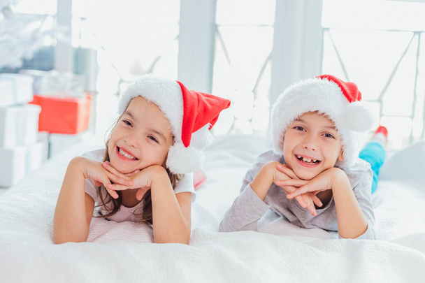 Close-up portrait of a little girl and boy in Christmas morning against white background of a New Year tree. - Foto, imagen