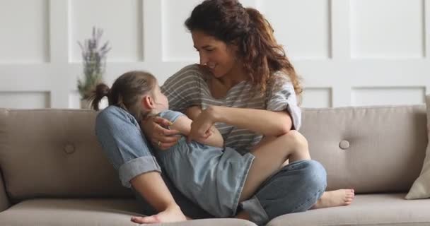 Cheerful young mum playing tickling cute kid daughter on sofa - Video