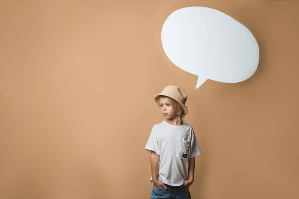 A boy in a hat stands on an orange background and shows different emotions. The boy is very happy. Of the boy there is an empty white speech - Foto, immagini