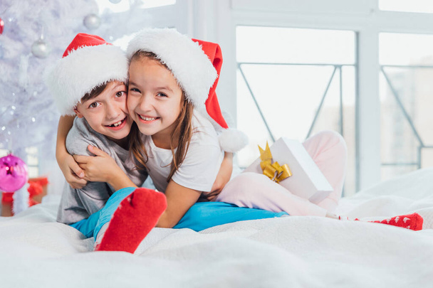 Two young happy cute laughing children, boy and girl, brother and sister having fun in the morning near Christmas tree. - Zdjęcie, obraz
