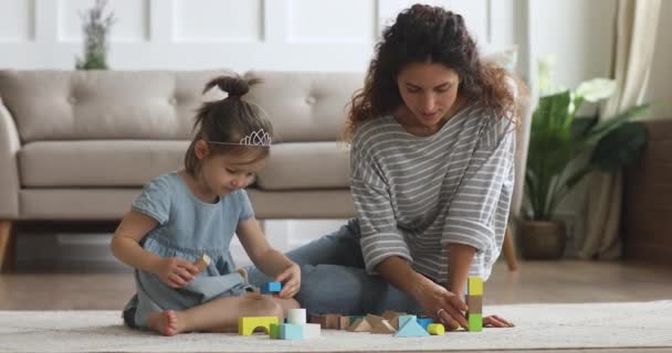 Happy mum helping child daughter building castle of wooden blocks - Video, Çekim