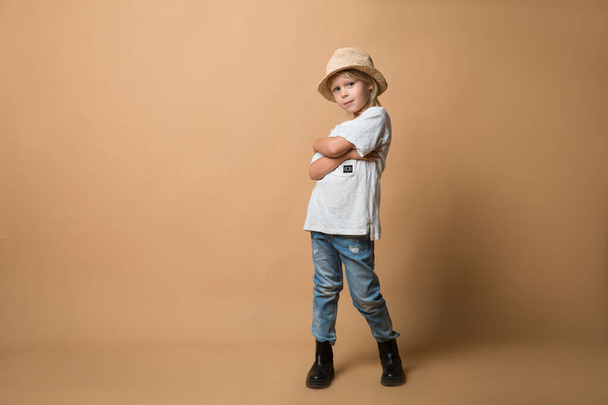 A boy in a hat stands on an orange background and shows different emotions. The boy is very happy - Φωτογραφία, εικόνα