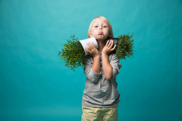Ένα μικρό αγόρι που κρατάει γλάστρες με ένα πράσινο φυτό. Παιδιά και φύση. Διατήρηση της φύσης - Φωτογραφία, εικόνα