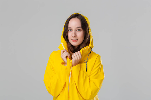 Hymyilevä ruskeaverikkö tyttö keltaisessa sadetakissa. Valmistaudu huonoon säähän.
. - Valokuva, kuva