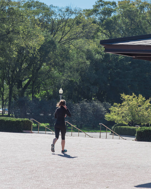 Fitness lady with fall sportswear and headphone running in Chicago park - Фото, изображение