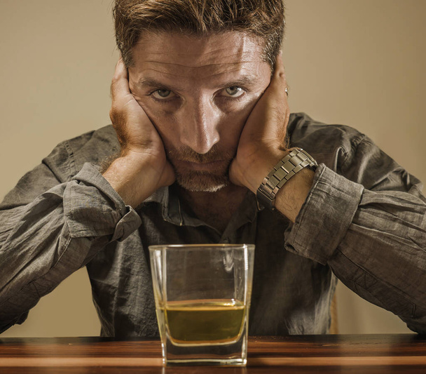 depressed and thoughtful alcoholic man on his 40s in front of whiskey glass wasted and stressed holding on temptation to drink in alcohol addiction and alcoholism problem - Zdjęcie, obraz