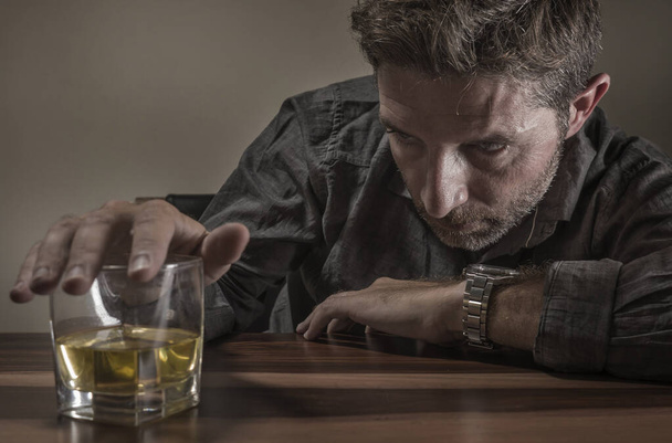 depressed and thoughtful alcoholic man on his 40s in front of whiskey glass wasted and stressed holding on temptation to drink in alcohol addiction and alcoholism problem - Photo, image