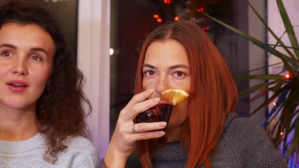 Κορίτσια με ένα ποτήρι κρασί επικοινωνούν σε ένα εορταστικό πάρτι. Ευτυχισμένοι φίλοι μαζί. Δύο νεαρές γυναίκες γιορτάζουν την παραμονή της Πρωτοχρονιάς στο σπίτι. Διακοπές και εορταστική έννοια. Βίντεο 4k Κοντινό πλάνο - Πλάνα, βίντεο