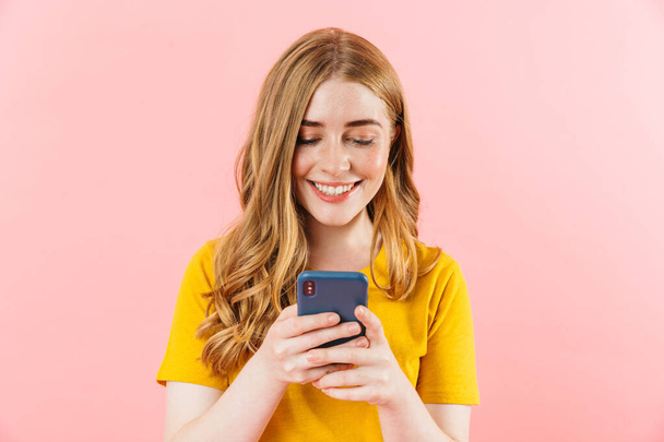Young cheery smiling happy cute girl isolated over pink wall background using mobile phone. - Foto, afbeelding