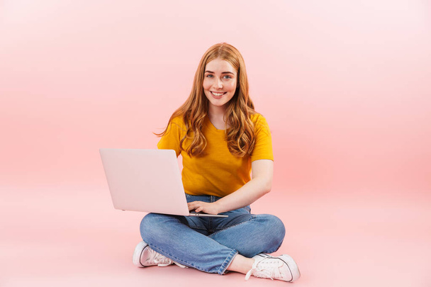 Positive smiling cheery girl isolated over pink wall background using laptop computer. - Valokuva, kuva