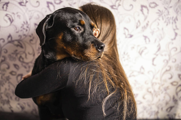 girl in a black jacket hugs a black dog on a background of patterned wall - Foto, Imagen