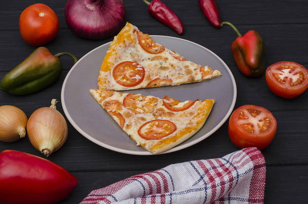 Sliced pizza with cheese and tomatoes on a gray plate with ingredients on a black wooden background. For menus and advertising pizzerias - Foto, Imagen